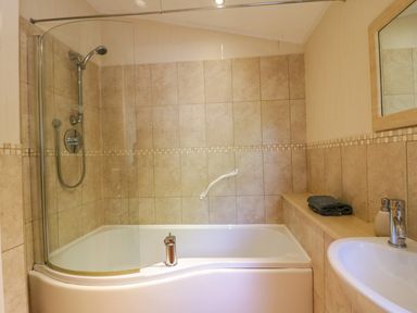 A bathroom with a bathtub and showerhead tiled walls and a sink with a mirror at The Hide Out Aldeburgh