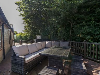 An outdoor patio area with wicker furniture including a corner sofa and table surrounded by trees at The Hide Out in Aldeburgh