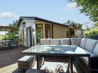 A wooden deck with outdoor seating including a glass table and cushioned wicker sofa outside a beige house at The Hide Out in Aldeburgh