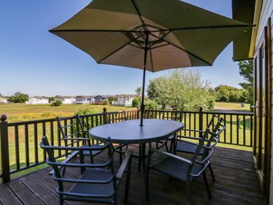 An outdoor deck with table chairs and an umbrella overlooking grass and houses at The Hide Out Aldeburgh
