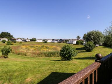 A grassy area with bushes and a flower patch in front of several small houses at The Hide Out in Aldeburgh
