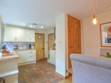 A kitchen with white cabinets and wooden doors and a dining area with upholstered chairs at Chapel Cottage Newbourne Near Woodbridge