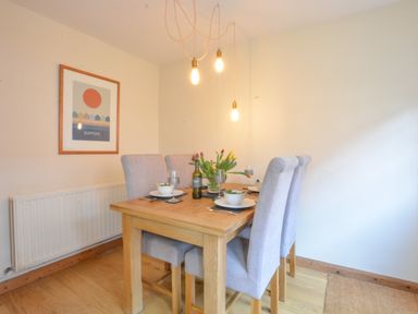 A dining area with a wooden table set for four with gray upholstered chairs and hanging pendant lights at Chapel Cottage Newbourne