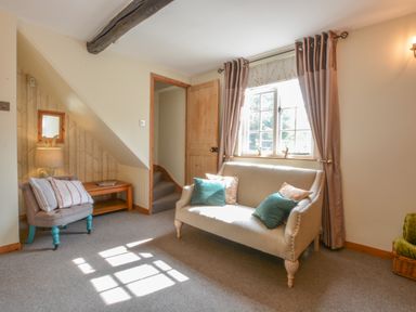 A sitting room with a beige sofa and blue cushions near a window with curtains at Chapel Cottage Newbourne Near Woodbridge