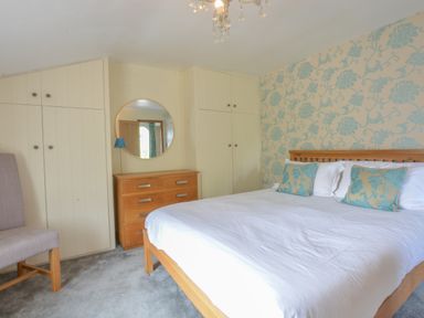 A bedroom with a bed pillows a dresser with a round mirror built in closets and a chair at Chapel Cottage Newbourne Near Woodbridge