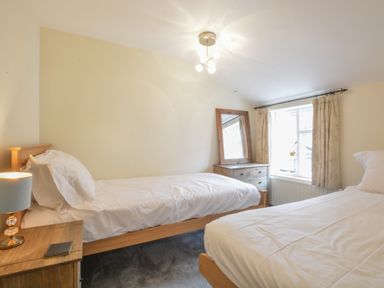 A bedroom with two single beds a wooden nightstand with a lamp and a notebook a wooden dresser with a mirror and a window with curtains at Chapel Cottage Newbourne Near Woodbridge