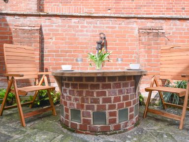 An outdoor seating area with two wooden chairs and a round brick table with flowers on top at Chapel Cottage Newbourne Near Woodbridge