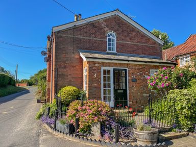 A brick cottage with a black door and flowering plants in front at Chapel Cottage Newbourne Near Woodbridge