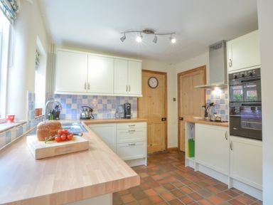 A kitchen with wooden countertops and cabinets with bread and tomatoes on the counter at Chapel Cottage Newbourne Near Woodbridge