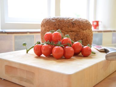A cutting board with a loaf of bread and a bunch of cherry tomatoes in a kitchen