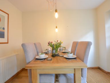 A dining room with a wooden table set for four with bowls salads wine glasses a bottle of wine and flowers at Chapel Cottage Newbourne Near Woodbridge
