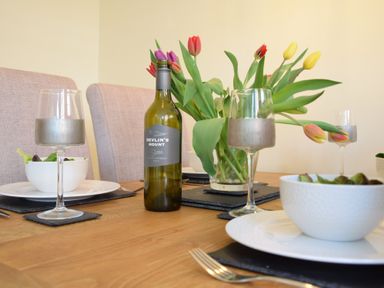 A dining table with a bottle of wine bowls of salad wine glasses and a vase of tulips at Chapel Cottage Newbourne Near Woodbridge