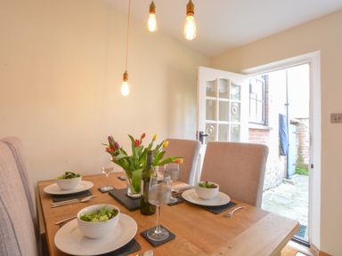 A dining room with a wooden table set with bowls of salad wine glasses and a vase of tulips at Chapel Cottage Newbourne Near Woodbridge