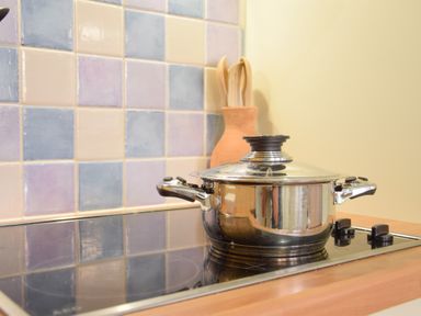 A stainless steel pot with lid on a stovetop with colorful tiled backsplash and wooden utensils in a holder at Chapel Cottage Newbourne Near Woodbridge