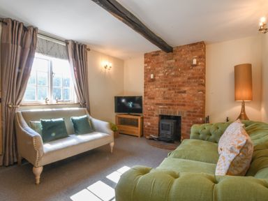 A living room with green and beige sofas a brick fireplace and a television at Chapel Cottage Newbourne Near Woodbridge