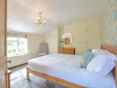 A bedroom with a wooden bed a dresser with a round mirror a chair and built-in wardrobes at Chapel Cottage Newbourne Near Woodbridge