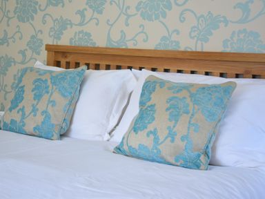 A bed with wooden headboard and decorative blue floral pillows at Chapel Cottage in Newbourne Near Woodbridge