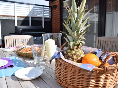 A wooden outdoor table with a basket of fruit and plates at Regatta Lookout in Aldeburgh