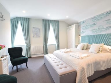 A bedroom with a large bed a bench two chairs and curtained windows at Regatta Lookout in Aldeburgh