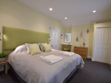 A bedroom with a bed with green headboard and pillows a dresser a vanity table with a chair and a closet at Regatta Lookout in Aldeburgh