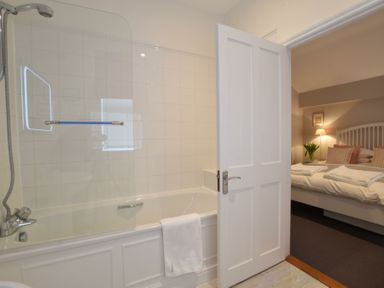 A bathroom with a bathtub and a shower screen next to a bedroom with a bed and bedside lamp at Regatta Lookout in Aldeburgh