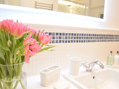 A bathroom sink with a chrome faucet pink flowers in a glass vase and toiletry holders at Regatta Lookout in Aldeburgh