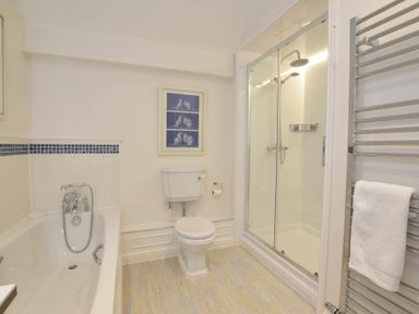 A bathroom with a bathtub toilet framed pictures shower and towel rack at Regatta Lookout in Aldeburgh