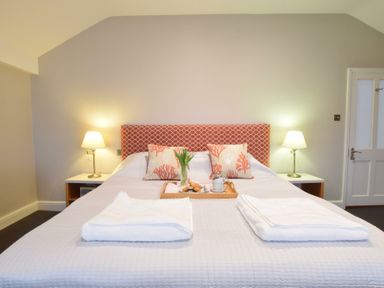 A bedroom with a double bed two bedside tables with lamps and a wooden tray with breakfast items on the bed at Regatta Lookout in Aldeburgh