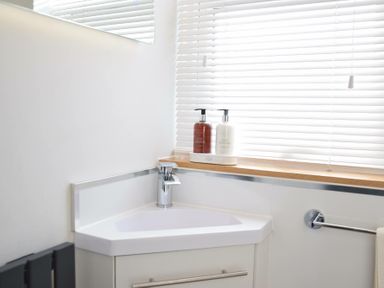 A corner bathroom sink with a faucet hand soap and lotion dispensers on the windowsill at Regatta Lookout in Aldeburgh