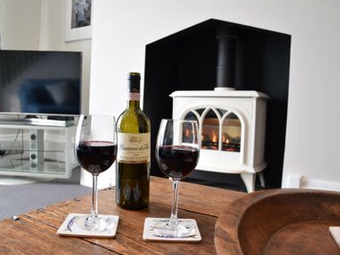 A bottle of red wine and two filled wine glasses on a wooden table in front of a white stove and television at Regatta Lookout in Aldeburgh