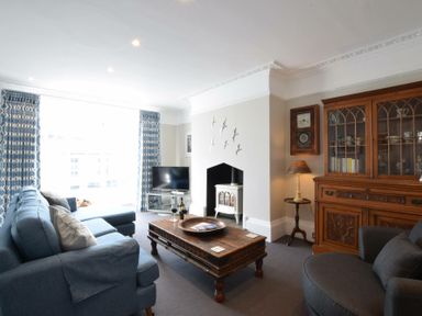 A living room with blue sofa wooden coffee table glass cabinet and wall-mounted clock at Regatta Lookout in Aldeburgh