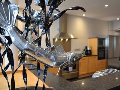 A metal fish sculpture on a kitchen counter with wooden cabinets and stainless steel appliances in the background at Regatta Lookout in Aldeburgh