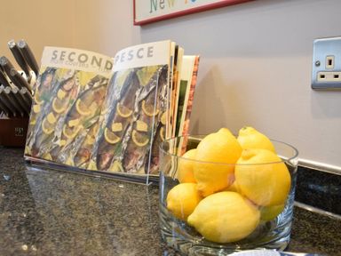 A kitchen counter with a glass bowl of lemons a cookbook open to a fish recipe and a knife block nearby at Regatta Lookout in Aldeburgh