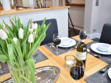A dining table set with wine glasses plates and a vase of tulips at Regatta Lookout in Aldeburgh