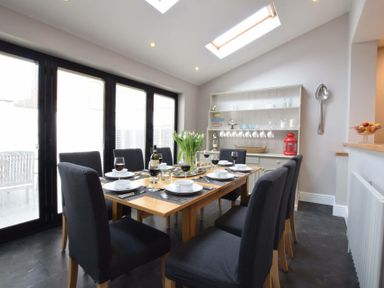 A dining room with a wooden table set for eight with black chairs and a hutch with cups and decorations at Regatta Lookout in Aldeburgh