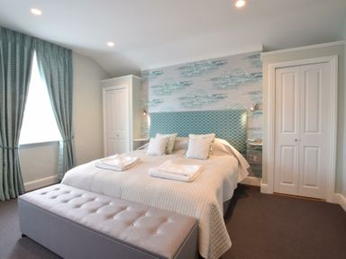 A bedroom with a double bed two wardrobes and a window with curtains at Regatta Lookout in Aldeburgh