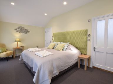 A bedroom with a bed with a green patterned headboard and a lamp on a small table at Regatta Lookout in Aldeburgh