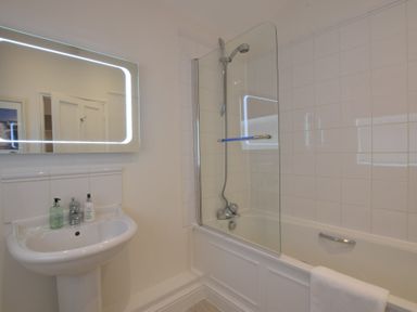 A bathroom with a pedestal sink and a bathtub with a glass shower screen at Regatta Lookout in Aldeburgh