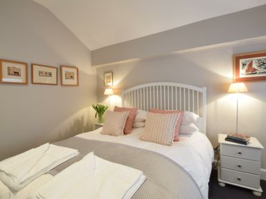 A bedroom with a double bed with pillows and towels and bedside tables with lamps and framed pictures on the walls at Regatta Lookout in Aldeburgh