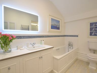 A bathroom with a sink cabinet mirror flowers bathtub and toilet at Regatta Lookout in Aldeburgh