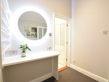 A room with a white desk and a round illuminated mirror above it with a small plant on the desk at Regatta Lookout in Aldeburgh