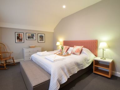 A bedroom with a bed a bench a rocking chair a chest of drawers and lamps at Regatta Lookout in Aldeburgh