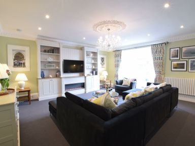 A living room with a black sofa a chandelier and a wall mounted television at Regatta Lookout in Aldeburgh