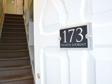 A stairway with carpet leading up and a white door with a sign showing 173 Regatta Lookout at Regatta Lookout in Aldeburgh