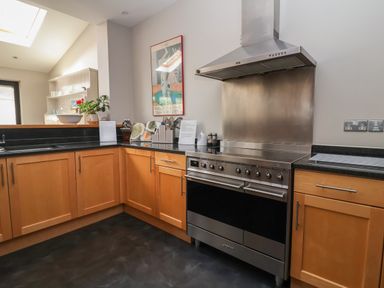 A kitchen with wooden cabinets black countertops a stainless steel stove and range hood at Regatta Lookout in Aldeburgh