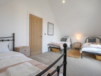 A bedroom with three single beds two bedside tables and a wooden door at Salt Marsh House Southwold