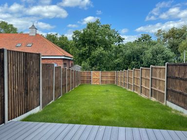 A backyard with green grass fenced with wooden panels and a wooden gate at Salt Marsh House Southwold