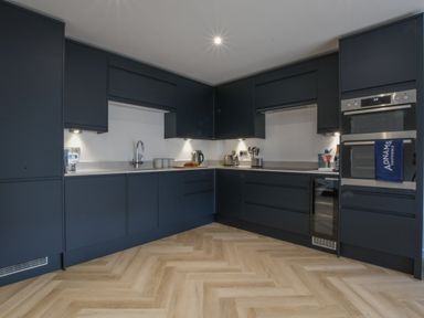 A kitchen with dark cabinets under and above a white countertop with a sink kettle toaster and built in ovens at Salt Marsh House Southwold