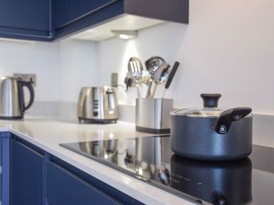 A kitchen countertop with a black pot on an induction stove a toaster kettle and kitchen utensils in a holder at Salt Marsh House Southwold