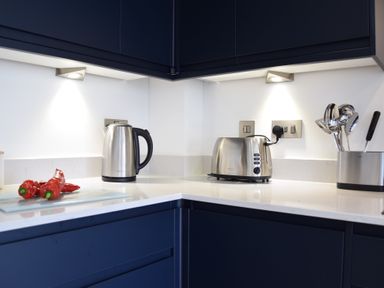 A kitchen corner with a stainless steel kettle toaster and utensils in holders on a white countertop at Salt Marsh House Southwold